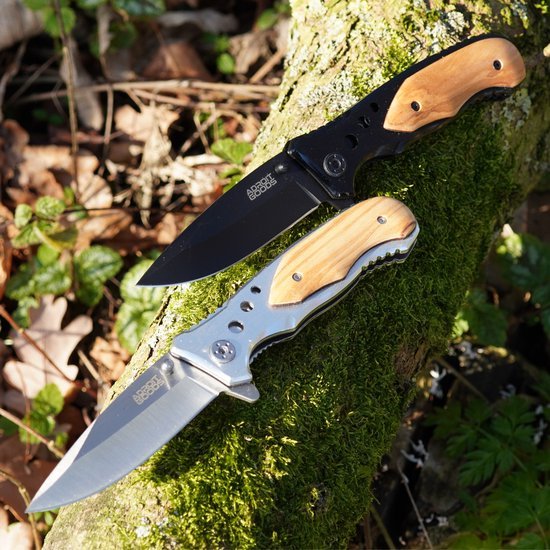 Twee inklapbare messen met houten handgrepen op een met mos bedekt boomstronk