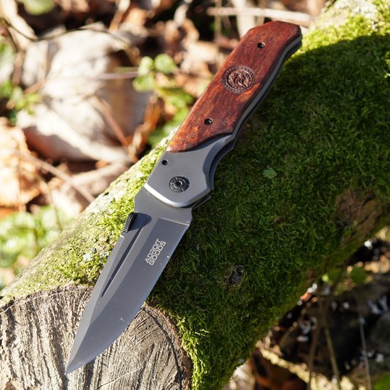 Zakmes met houten handgreep liggend op met mos bedekt hout in buitenomgeving