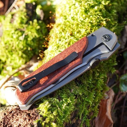 Opgevouwen zakmes met houten handgreep en metalen clip liggend op mos en boomschors