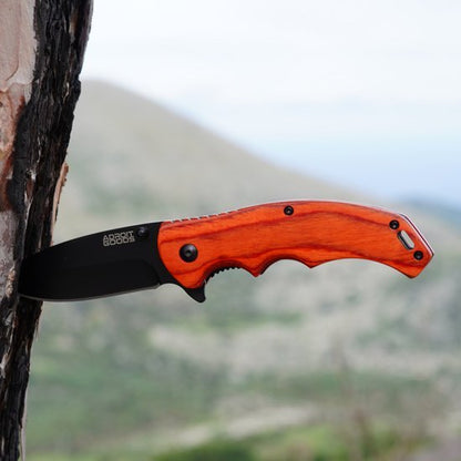 Opvouwbaar mes met zwarte kling en houten handvat bevestigd aan boomstam in natuurlijke omgeving