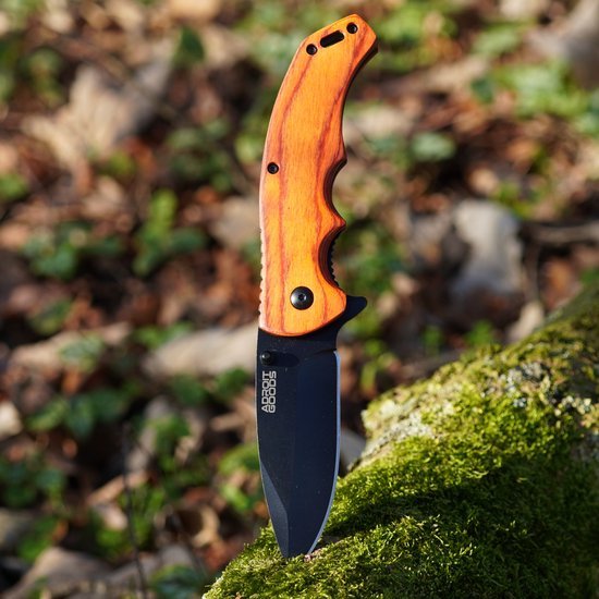 Opvouwbaar mes met houten handvat en zwart lemmet in natuurlijke buitenomgeving