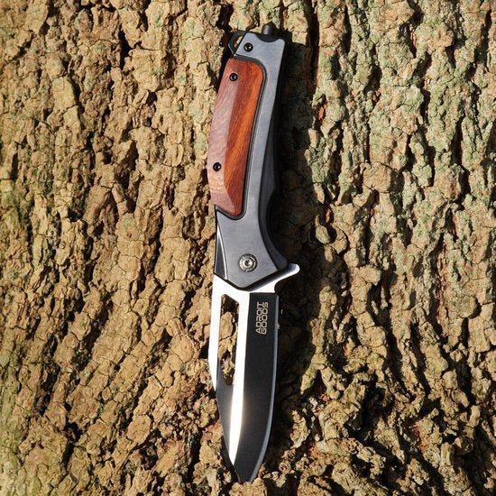 Opvouwbaar mes met houten handvat en zwart lemmet op boomschors achtergrond