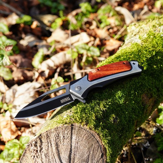 Opgevouwen mes met zwarte lemmet en houten handvat liggend op met mos bedekt boomstam