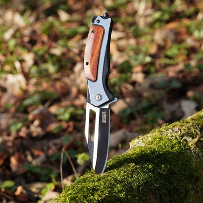 Opgevouwen mes met houten handvat en roestvrijstalen lemmet in een bosrijke omgeving