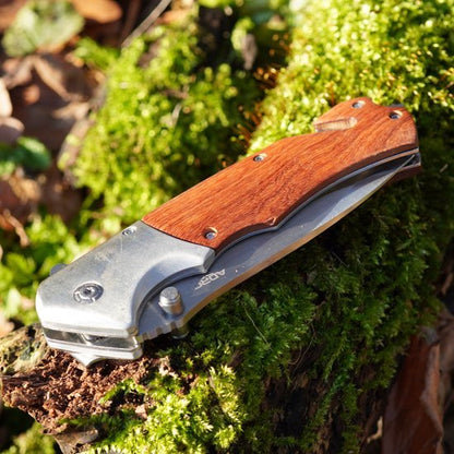 Opvouwbaar mes met houten handvat op groene mosachtige boomstronk in zonlicht