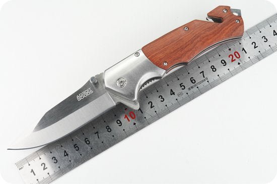 Opvouwbaar zakmes met houten handgreep en metalen lemmet boven een liniaal geplaatst.