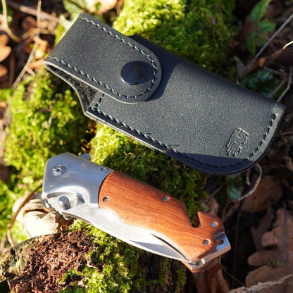 Opvouwbaar zakmes met houten handvat en leren beschermhoes op mosbedekte ondergrond