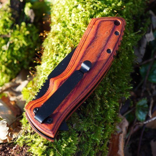 Inklapbaar mes met houten handvat en zwarte clip liggend op groene mosgrond in buitenomgeving