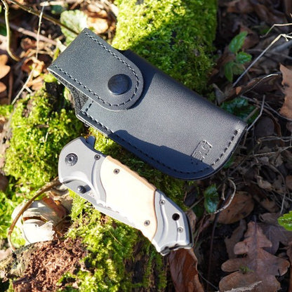 Zwarte leren schede met drukknoop en opgevouwen zakmes met licht houten handgreep buiten