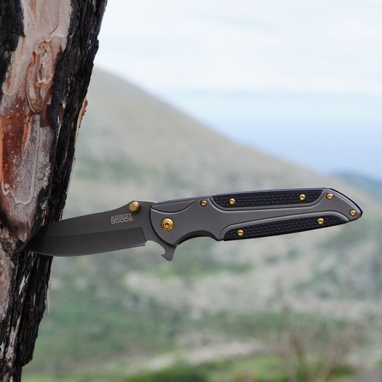 Opvouwbaar mes met zwart handvat en gouden details ingeboord in een boomstam in de natuur