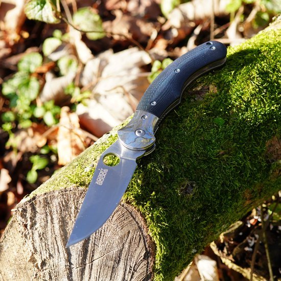 Opgevouwen zakmes met zwarte handgreep liggend op mosbedekt hout in de natuur