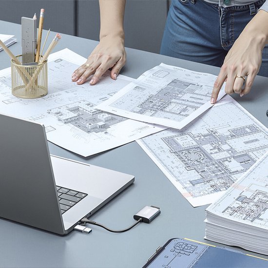 Handen die bouwtekeningen overlopen op een bureau met laptop en schrijfbenodigdheden