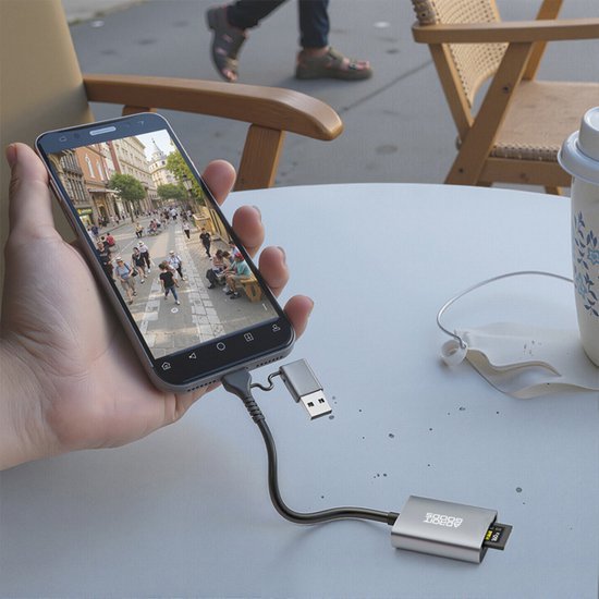 Hand houdt smartphone verbonden met USB-adapter op een tafel met koptelefoon en beker