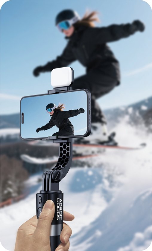 Hand die smartphone en lamp vasthoudt terwijl iemand sneeuwskiet op de achtergrond in actie