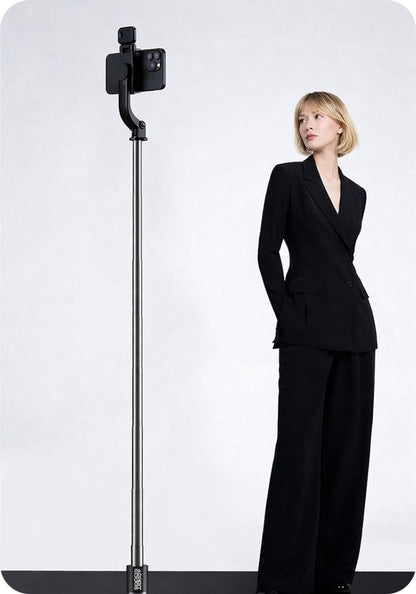 vrouw in zwart pak staand naast een lange selfiestick met smartphone en stabilisator