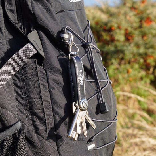 Zwarte rugzak met sleutelhanger en sleutels bevestigd aan een gesp buiten in de natuur.