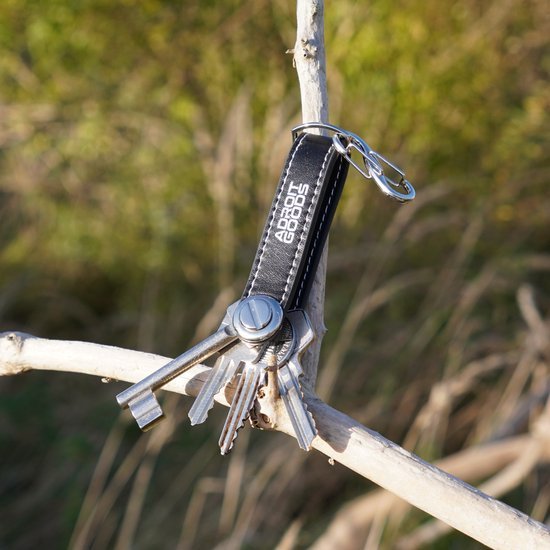 Zwarte sleutelhanger met metalen sleutels hangend aan tak in natuurlijk buitengebied