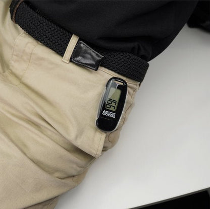 Zwart digitaal apparaatje met scherm en logo bevestigd aan beige broekzak naast zwarte riem