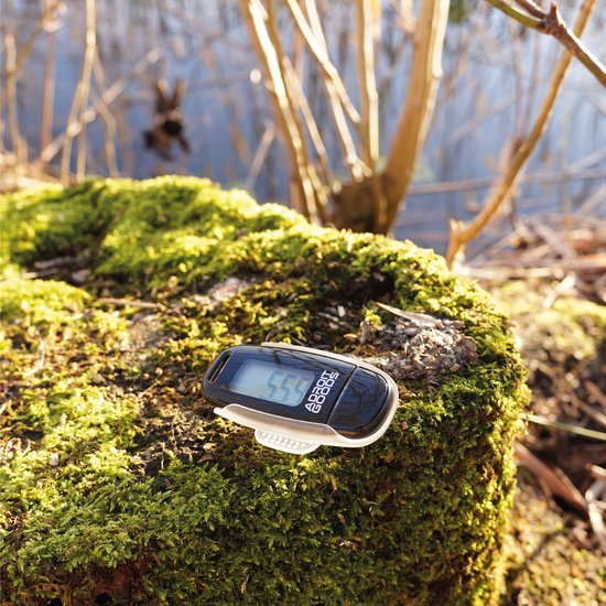 Fitness tracker met digitale display liggend op mos bedekt boomstronk in zonlicht