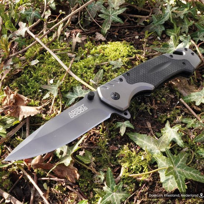 Openslaand mes met zwart handvat liggend op mos en bladeren in de natuur