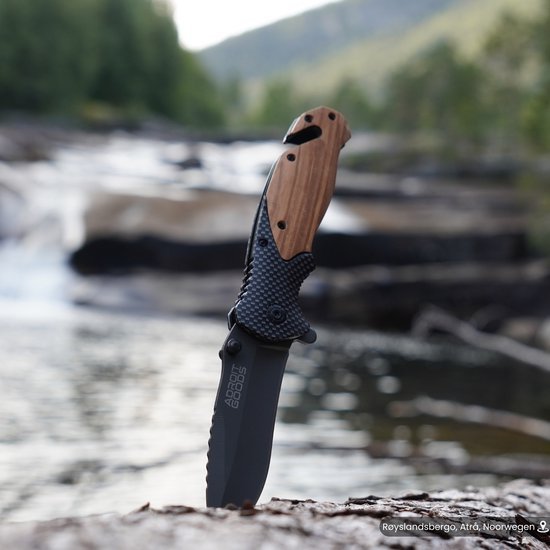 Opengeslagen zakmes met houten handvat in natuurlijke buitenomgeving bij stromend water.