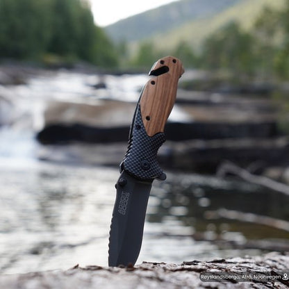 Opengeslagen zakmes met houten handvat in natuurlijke buitenomgeving bij stromend water.