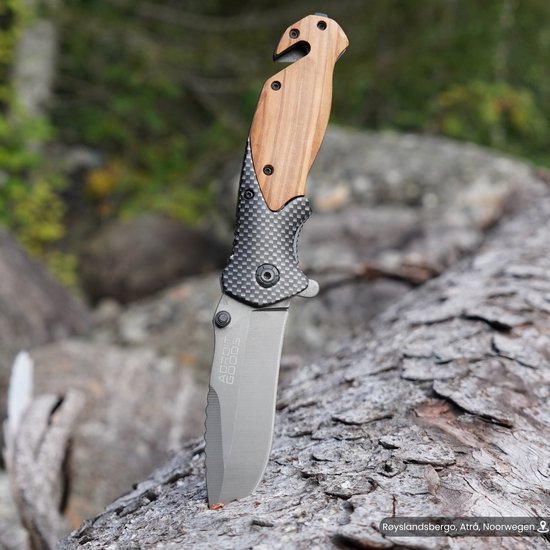 Opgevouwen mes met houten handgreep en metalen lemmet op boomstam in natuur.