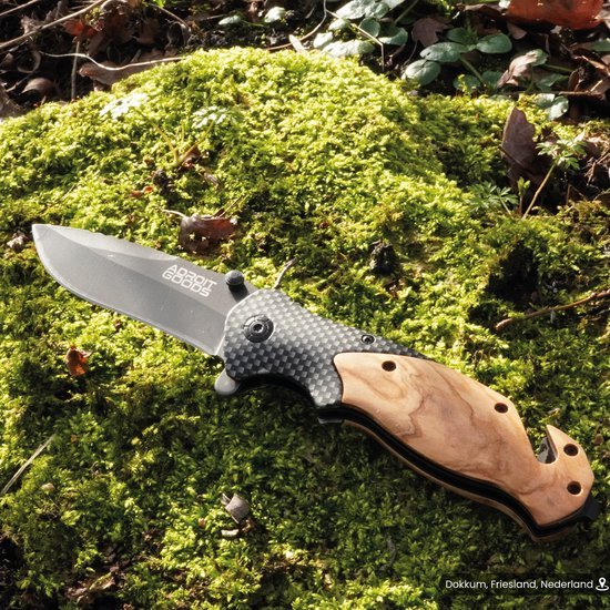 Vouwmes met houten handgreep en carbonfiber details liggend op mos in de natuur