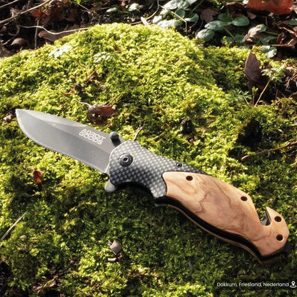 Vouwmes met houten handgreep en carbonfiber details liggend op mos in de natuur