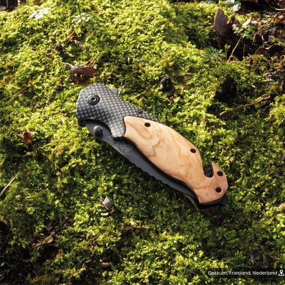 gevouwen zakmes met houten handvat en zwarte lemmet in mosrijke natuurlijke omgeving