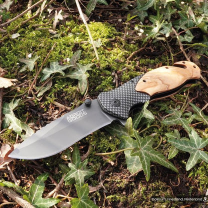 Jachtmes met licht houten handgreep en roestvrijstalen lemmet liggend op mos en bladeren