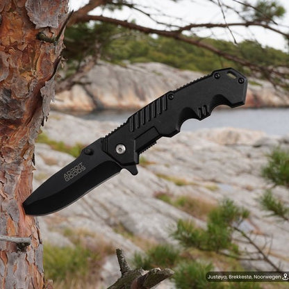 zwart opvouwbaar zakmes met zwart handvat, vastgeklemd aan boomstam in bosrijke omgeving