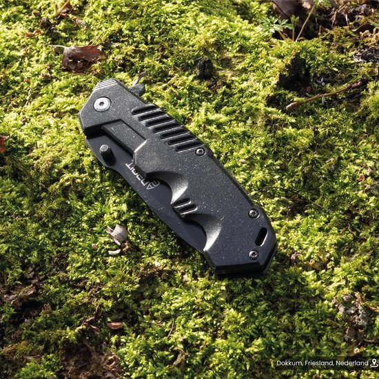 Gesloten zwart inklapbaar mes liggend op groen mos in buitenomgeving