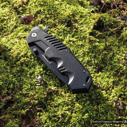 Gesloten zwart inklapbaar mes liggend op groen mos in buitenomgeving