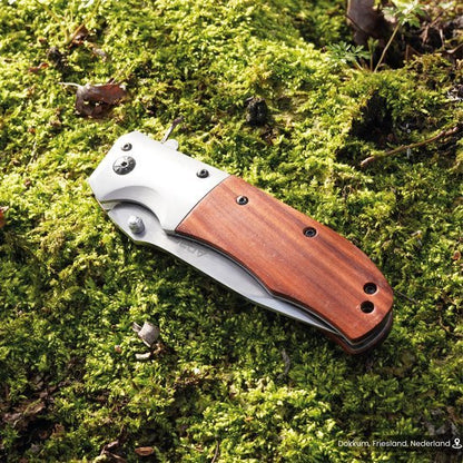 Opgevouwen zakmes met houten handvat liggend op groen mos in de buitenlucht