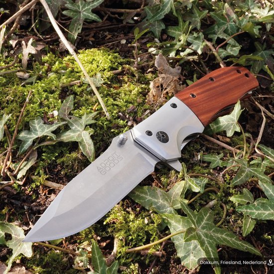 Vouwmes met houten handvat en scherp roestvrijstalen lemmet liggend op mos en bladeren