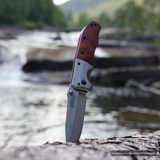 Stevig mes met houten handvat rechtop in rots bij rivier in natuuromgeving geplaatst