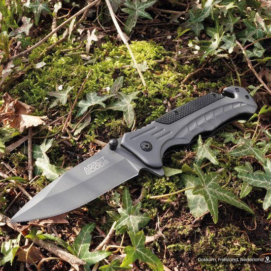 Opengeslagen vouwmes met zwart handvat liggend op groen mos en klimopbladeren