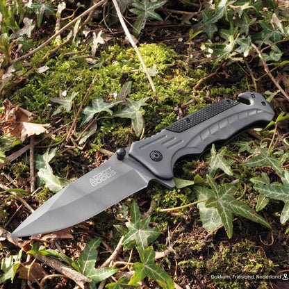 Opengeslagen vouwmes met zwart handvat liggend op groen mos en klimopbladeren