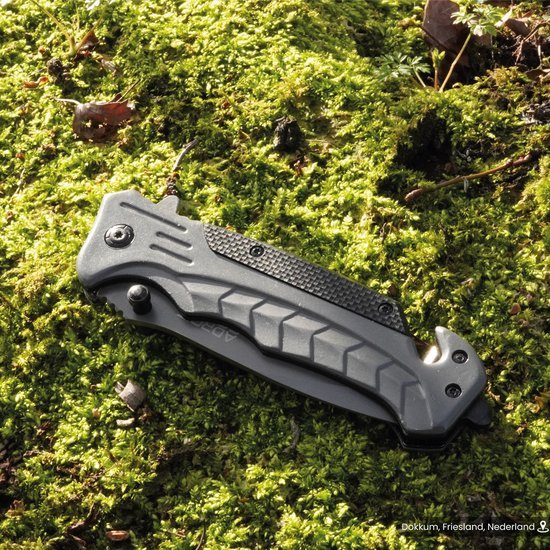 Opgevouwen grijs zakmes met zwarte details liggend op groene mosgrond in de natuur.