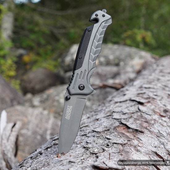 Openslaand mes met grijze handgreep steekt in een boomstam in een bosrijke omgeving