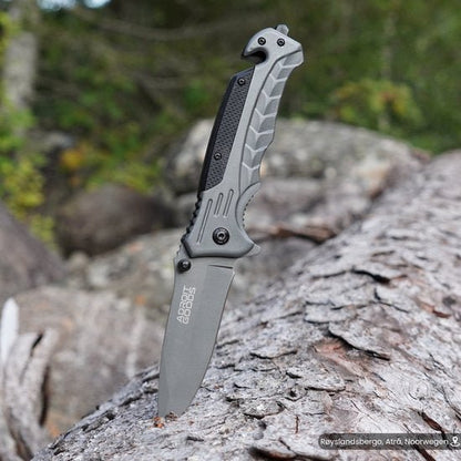 Openslaand mes met grijze handgreep steekt in een boomstam in een bosrijke omgeving