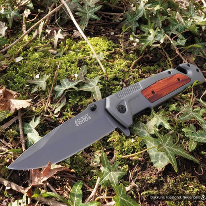 Opvouwbaar mes met houten handgreep en grijze lemmet op mos en klimop in de natuur