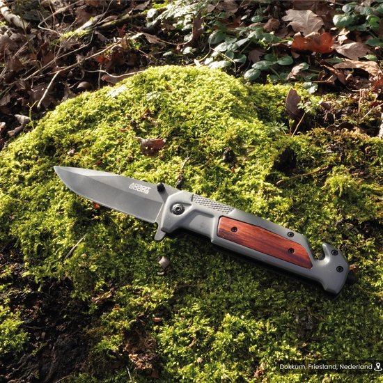 Vouwmes met houten handvat liggend op groen mos onder zonlicht in bosrijke omgeving