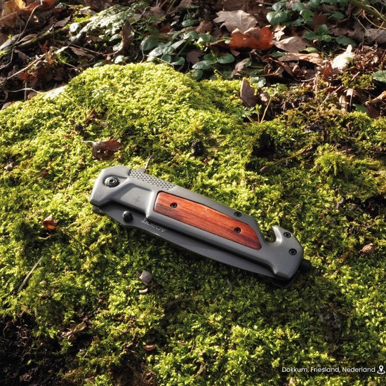 Opgevouwen zakmes met houten greep op mos bedekt bosgrond met bladeren eromheen