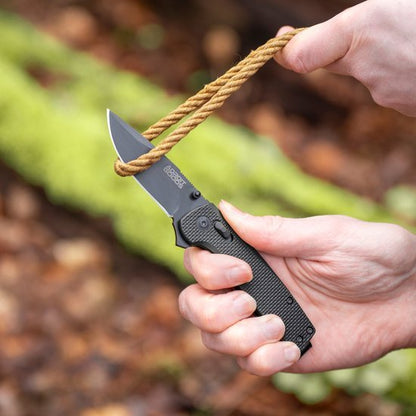 Hand gebruikt scherp mes om touw stevig door te snijden in buitenomgeving met groene achtergrond