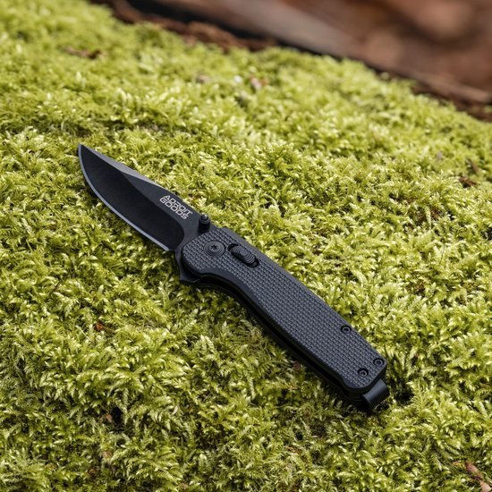 Opvouwbaar zwart mes met gegraveerd logo, liggend op groene mosachtige ondergrond
