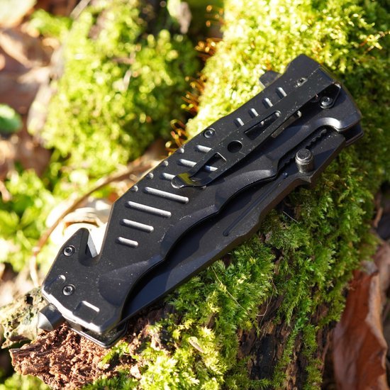 Zwarte inklapbare zakmes met riemclip liggend op groen mos en hout