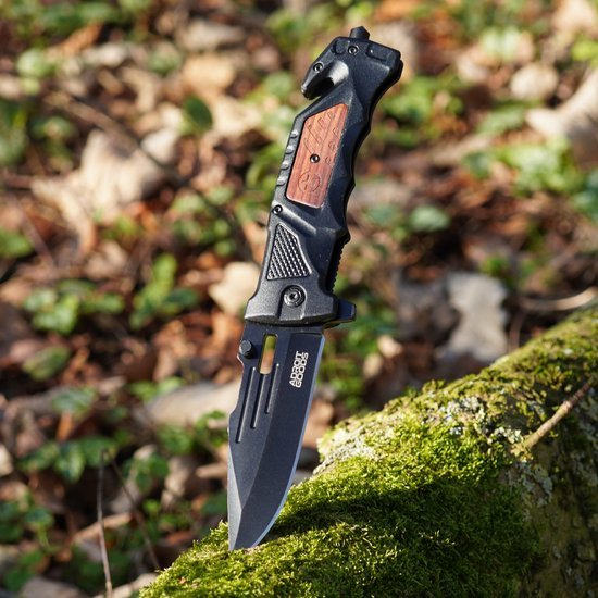 Stevige zwarte mes met houten handvat op mosbedekte boomstam in bosrijke omgeving