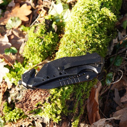 Opgevouwen zwart zakmes met clip ligt op een met mos bedekt stuk hout buiten in het bos